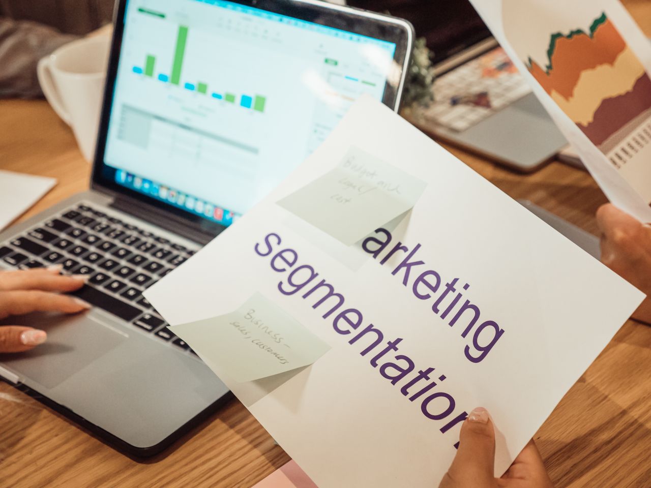A contemporary work environment featuring hands reviewing marketing data on a laptop and printed documents.